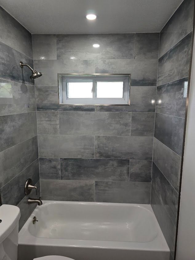 Bathroom with gray and blue tiled walls, a tub, and a small window