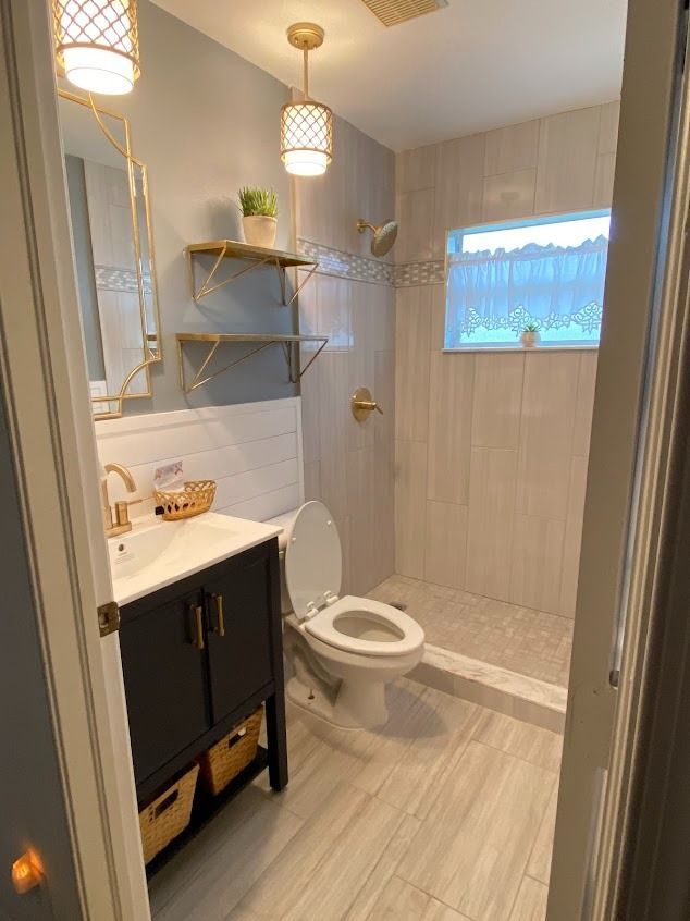 Bathroom with blue-gray walls, gold fixtures, black vanity, and a walk-in shower with a window