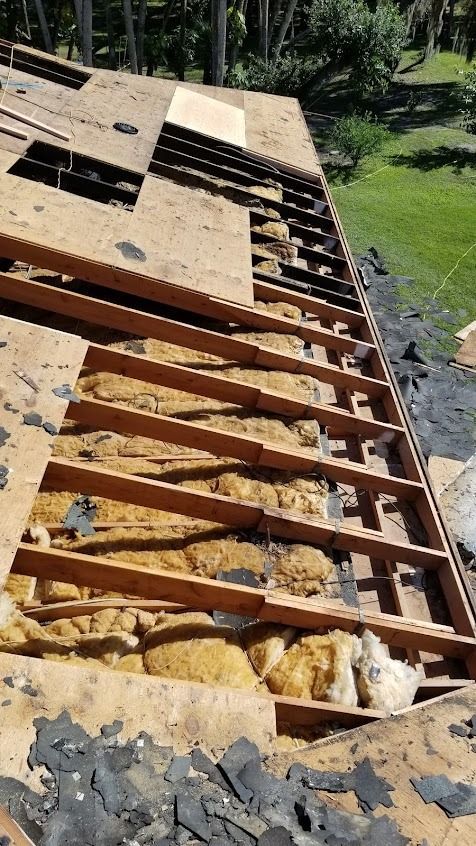 Roof being repaired; plywood removed, exposing rafters and insulation; asphalt shingle debris.