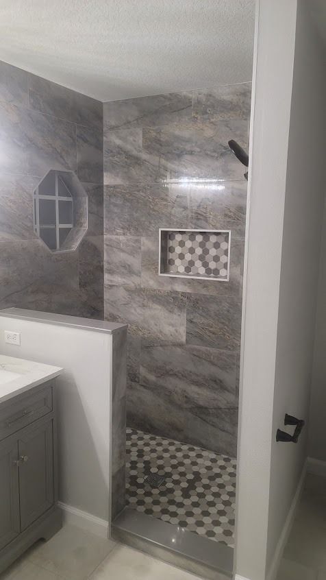Gray and white tiled shower with recessed shelves, hexagonal floor, and dark fixtures