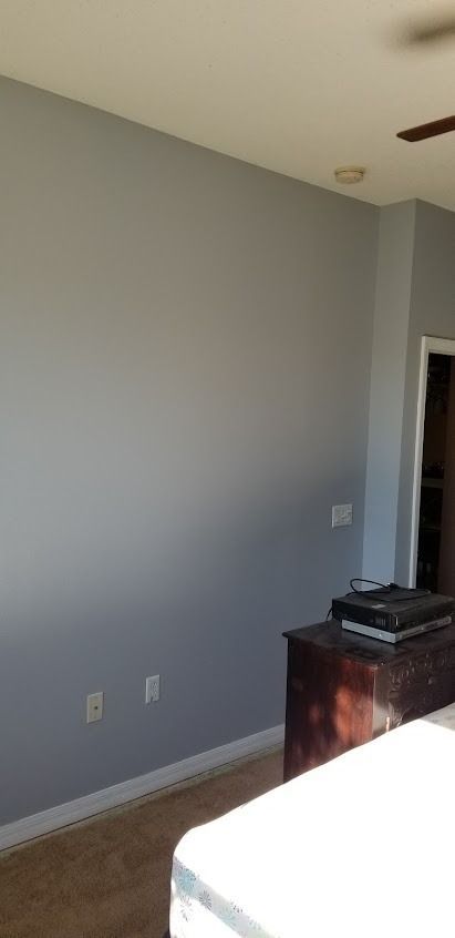 A bedroom wall painted gray with a chest of drawers and a bed in view