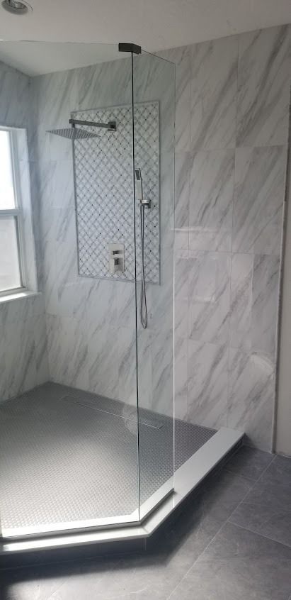 A modern shower with glass walls, gray tile floor and marble-like wall tiles
