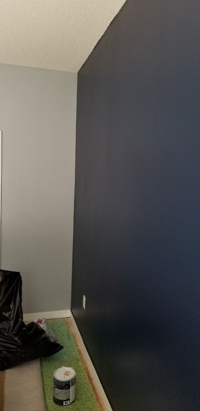 Room with navy and gray painted walls, paint can on green mat, and a black trash bag