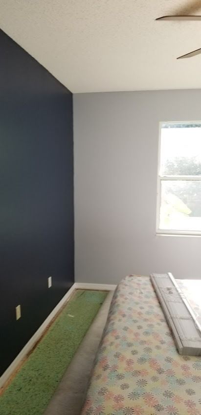 Bedroom with dark blue accent wall, light gray wall, and floral bedspread