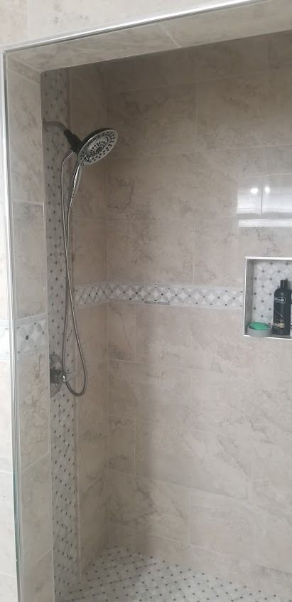 A beige-tiled shower stall with a showerhead and a built-in niche holding toiletries