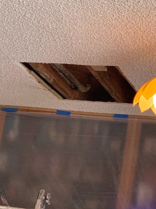 Hole in textured ceiling revealing wooden beams, with a light fixture in the corner