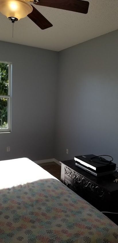 A bedroom with gray walls, a bed with a floral comforter, and a black chest of drawers