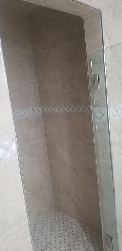 A shower with a glass door, tiled walls, and a decorative border