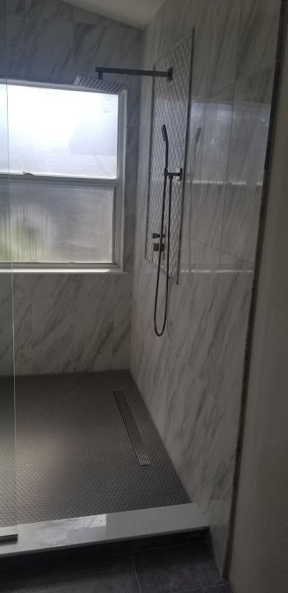 A modern shower with marble-like tile walls, a glass door, and a window