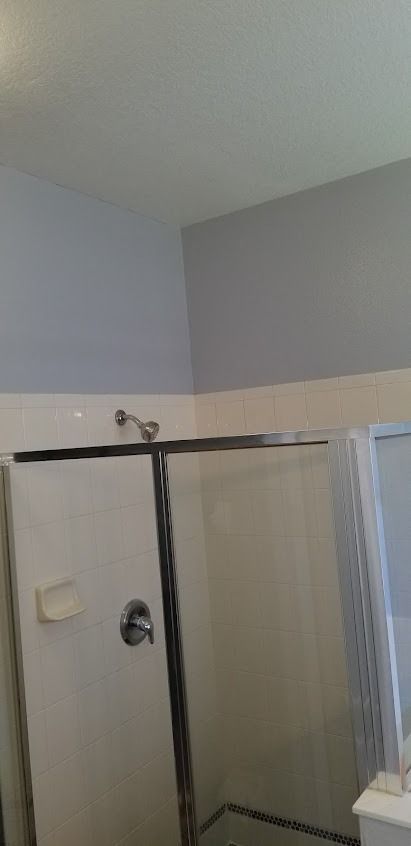 A bathroom with a glass shower door, silver fixtures, and light blue walls