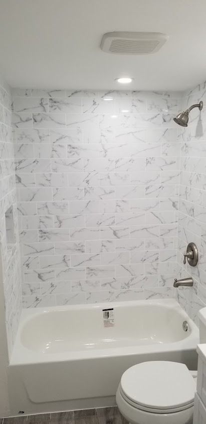 Bathroom with white bathtub, toilet, and marble-patterned shower wall