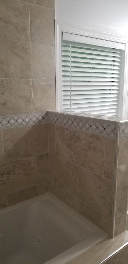 Bathroom with beige tiled walls, a bathtub, and a window with blinds