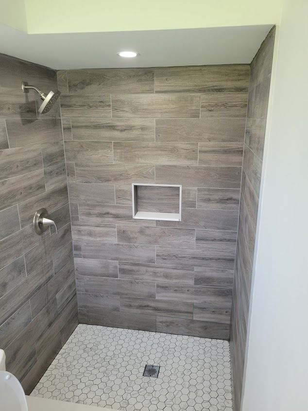 Tiled shower with wood-look walls, a built-in niche, and a white hexagon tile floor