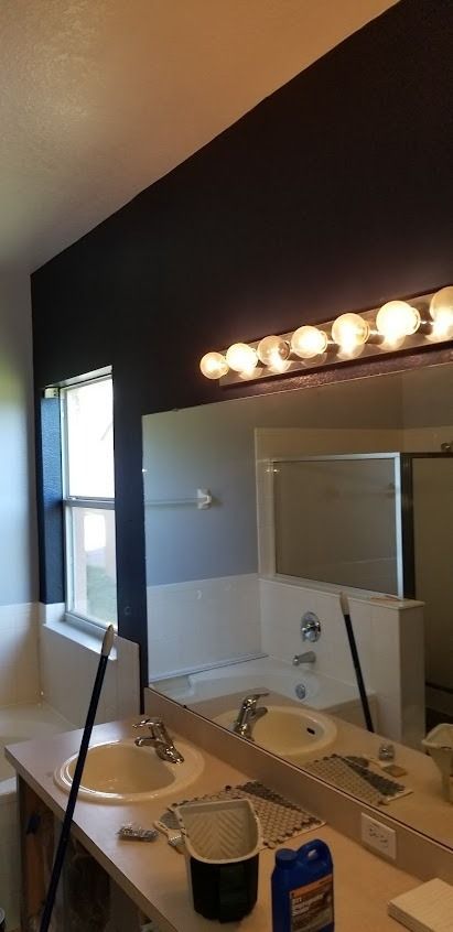 Bathroom with dark blue wall, vanity with two sinks, mirror, and bright light fixture.