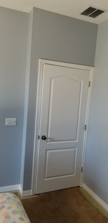 A white door set into a grey wall, framed by white trim. There's a light switch to the left.