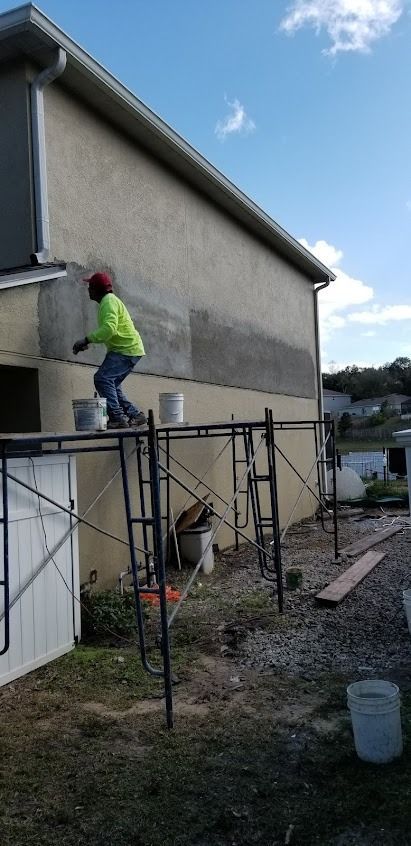 Construction worker on scaffolding applying stucco to a building exterior.