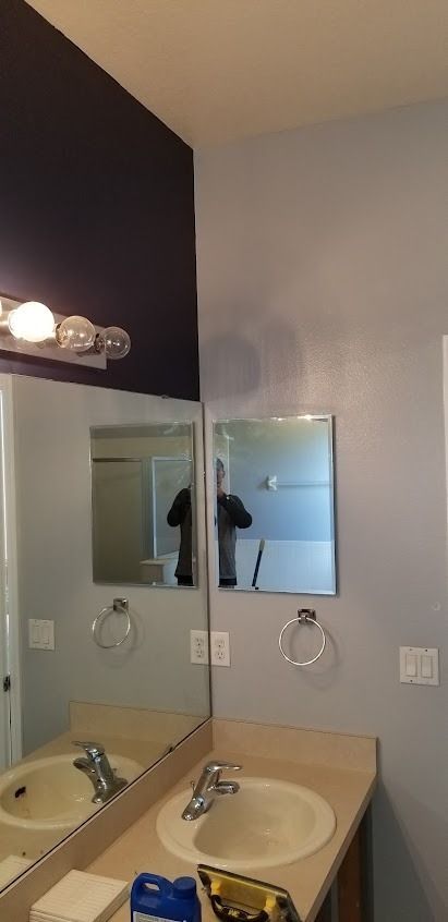 Bathroom with mirrors, sink, and toiletries, with a dark purple wall and light gray walls