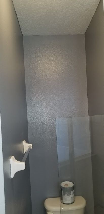 A small bathroom corner with gray walls, white ceiling, toilet, and paint can