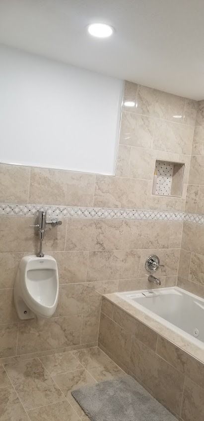 A bathroom with a urinal, bathtub, and beige tile walls