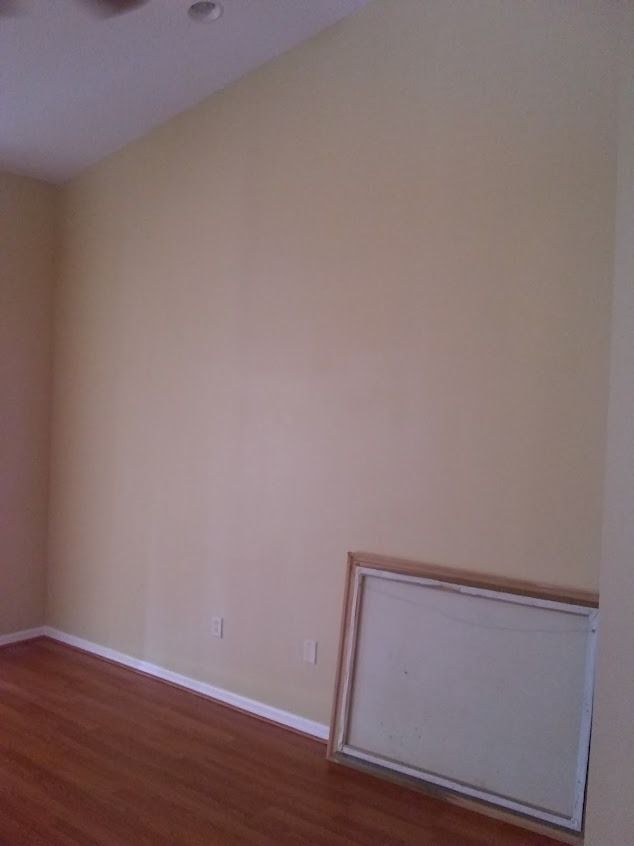 Empty room with pale yellow walls, hardwood floors, and a leaning rectangular frame