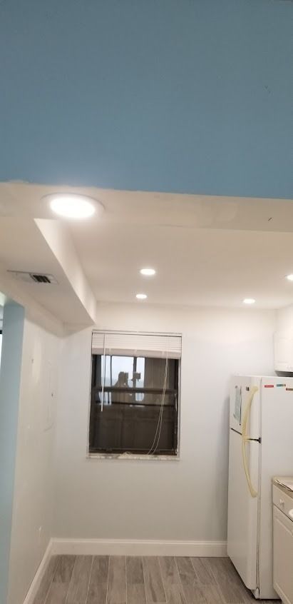 Interior of a kitchen with blue ceiling and white walls, includes a window and refrigerator