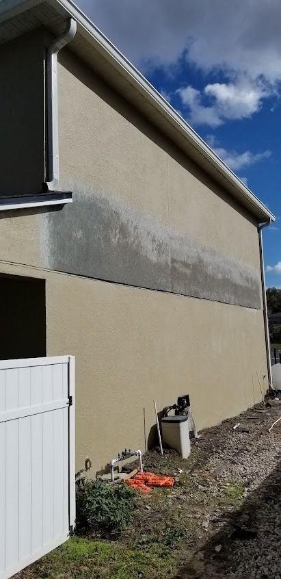 Exterior of a tan stucco building with water damage and a white fence in the foreground