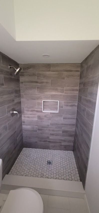 Bathroom shower with gray tiled walls, stone floor, and shower head