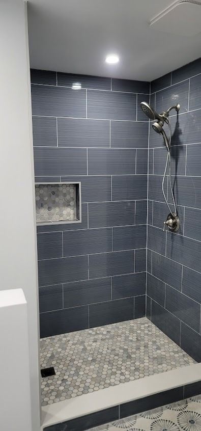 Modern shower with dark gray tile walls, pebble-stone floor, and a built-in niche