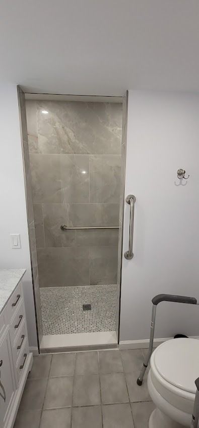 Bathroom with a walk-in shower, toilet with a grab bar, and white vanity