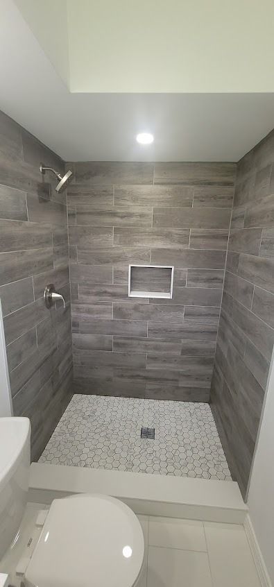 A modern shower with gray tile walls, mosaic floor, and toilet.