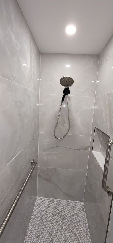A modern shower with grey tile walls, a large showerhead, and a small pebble floor.