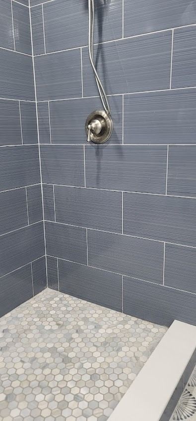 Shower with gray tiled walls, a mosaic tile floor, and a chrome shower head