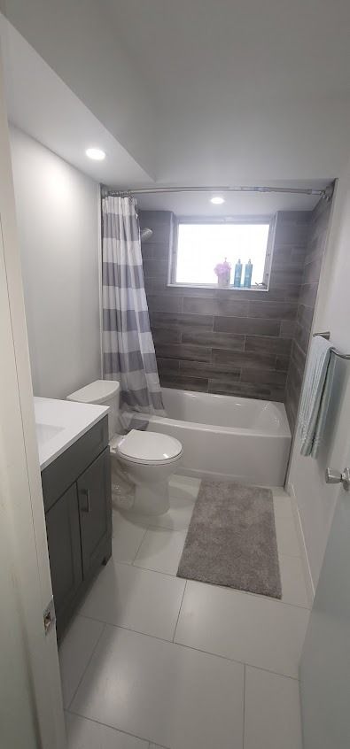 Bathroom with white tiles, gray vanity, toilet, tub, and a gray wooden accent wall