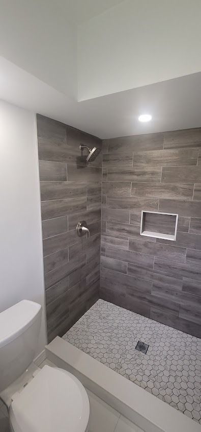Bathroom with gray tile shower and toilet. Shower floor is white and gray small tiles
