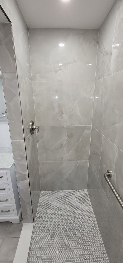 A walk-in shower with grey tiles, pebble floor, and a handrail