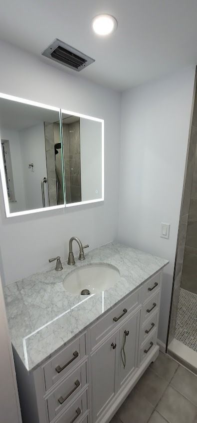Bathroom with a white vanity, marble countertop, illuminated mirror, and silver faucet