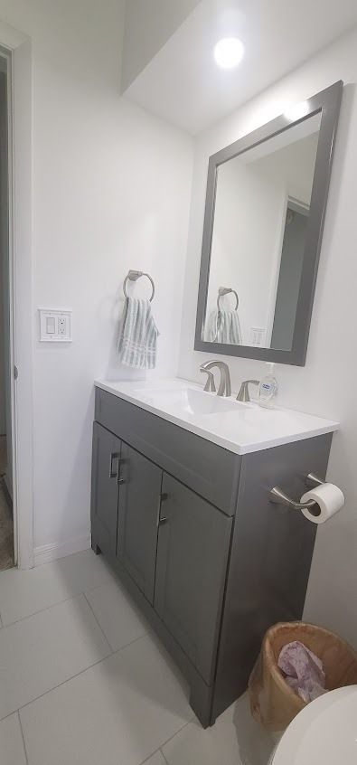 Bathroom with gray vanity, white countertop, mirror, towel, and toilet paper roll