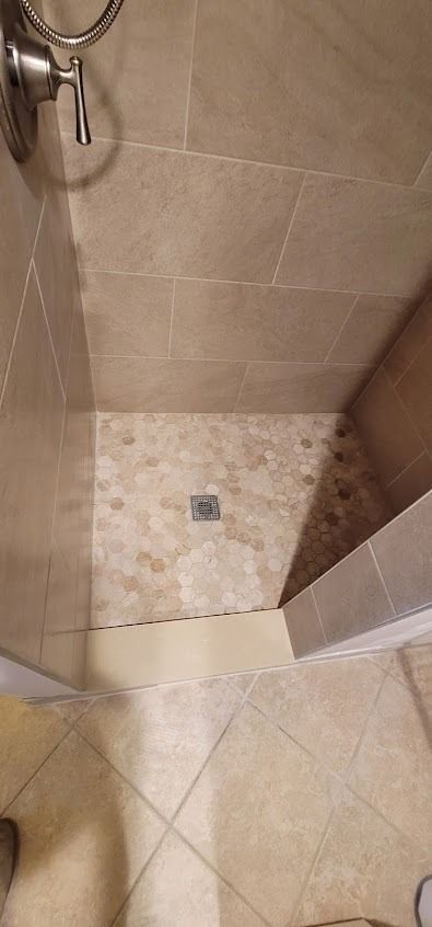 Shower with beige tile walls and a stone-tiled floor, seen from an elevated perspective