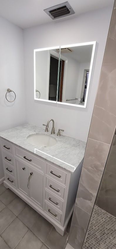 Bathroom with white vanity, marble countertop, lighted mirror, and chrome fixtures