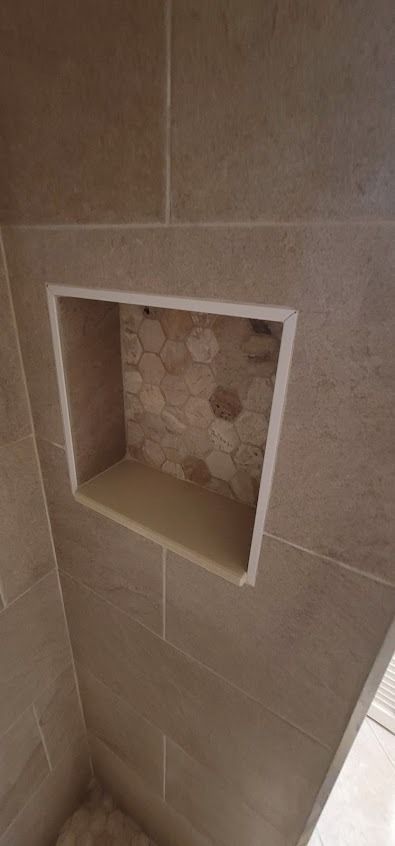 Bathroom wall with a built-in shelf. The shelf is framed in white, and the back is tiled with pebbles