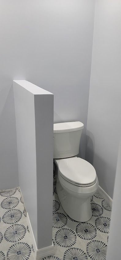 A toilet in a small bathroom, with a white partition and patterned floor tiles