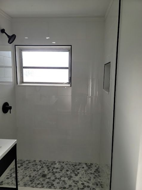 White tiled shower with pebble floor, black fixtures, and small window