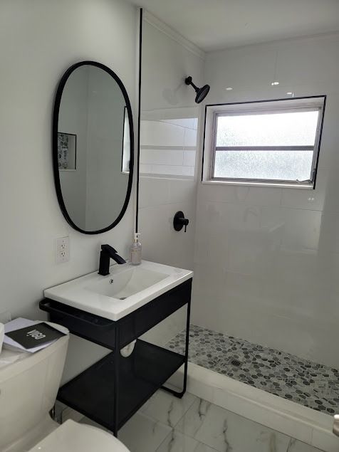 Modern white bathroom with black fixtures and a black-framed oval mirror