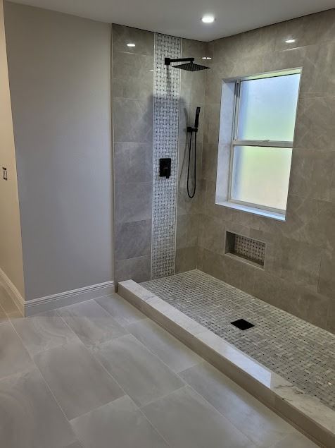 Modern bathroom with stone-tiled walls and floor, black shower fixtures, and a window