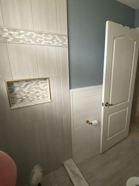 Bathroom remodel: tiled shower wall with niche, decorative tile band, door, and light blue wall