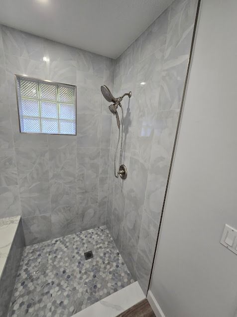 Gray-tiled shower with pebble floor, glass block window, and silver showerhead