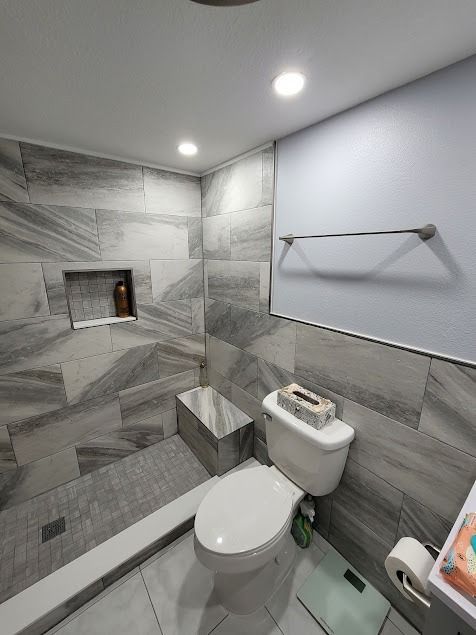 Gray tiled bathroom with shower, toilet, and built-in bench