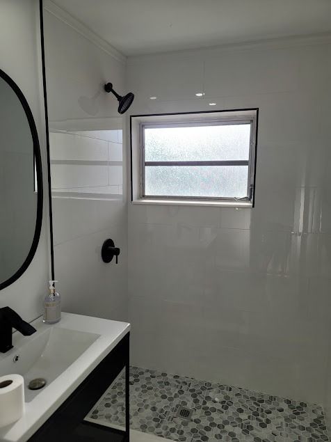 Bathroom with white tile, black fixtures, pebble floor, and a small window