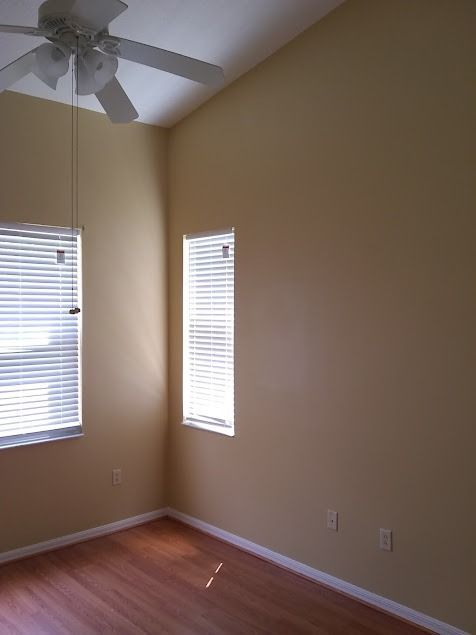 Bedroom corner with light tan walls, two windows with blinds, and a ceiling fan