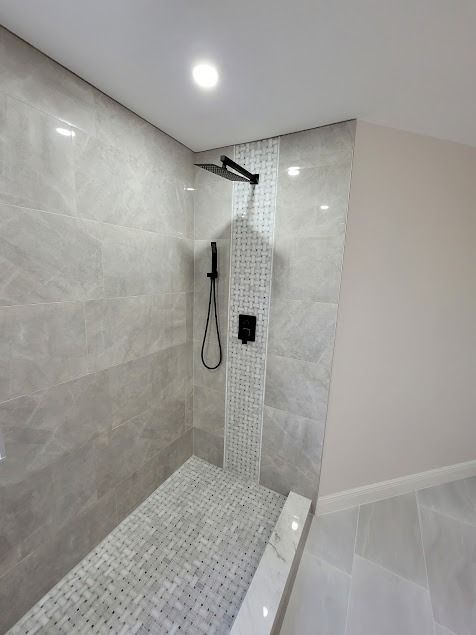 Modern shower with gray tile walls, black fixtures, and mosaic floor